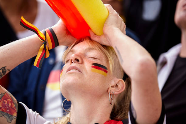 Frustrated German football fan holding her head at Germany national team game Mid-shot of frustrated German football fan with painted face and German colors ribbon on wrist holding her head at Germany national team game women under 20 stock pictures, royalty-free photos & images