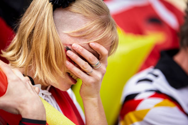 Frustrated German woman covering her face with hand at Germany national team match Mid-shot of frustrated German football fan covering her face face with hand in crowded stadium at Germany national team match women under 20 stock pictures, royalty-free photos & images