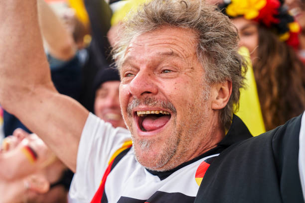 Happy middle age German football supporter chanting and cheering for national team Medium shot of happy middle age German football supporter wearing Germany national team jersey chanting and cheering for team in crowded stadium women under 20 stock pictures, royalty-free photos & images