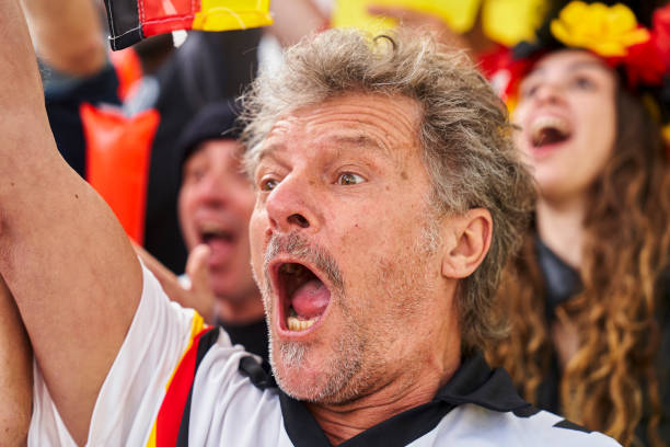 Excited mature German football fan celebrating after team scores goal in crowded stadium Mid-shot of excited mature German football fan wearing Germany national team jersey celebrating after team scores goal in crowded stadium women under 20 stock pictures, royalty-free photos & images