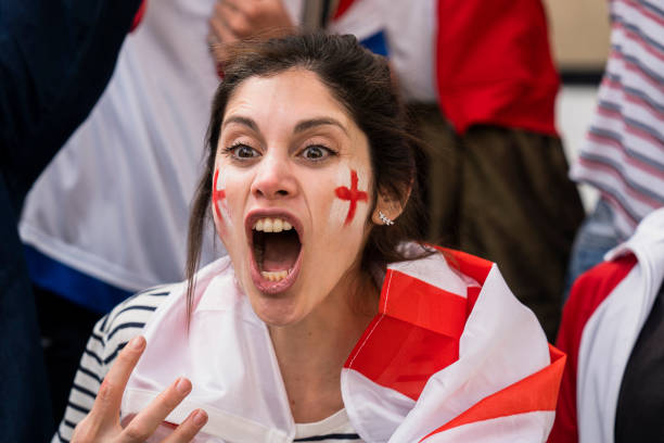 Young English woman cheering for England's national team in crowded stadium Mid-shot of young excited English woman with white and red face paint chanting and cheering for England's national team in crowded stadium women under 20 stock pictures, royalty-free photos & images
