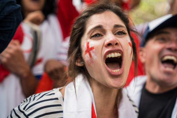 English football fan with English flag wrapped around her neck cheering for national football team Mid-shot of English football wearing an English flag around her neck and white and red face paint chanting for national football team chanting stock pictures, royalty-free photos & images