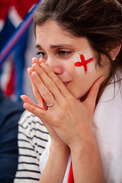Sad young English football fan wearing England flag around her neck about to cry during national team match Medium shot of sad English football fan wearing England flag around her neck and white and red face paint about to cry after national team fails to win match in crowded stadium women under 20 stock pictures, royalty-free photos & images