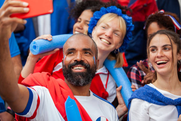 Happy group of male and female French football fans taking selfies at France's national team game stock photo