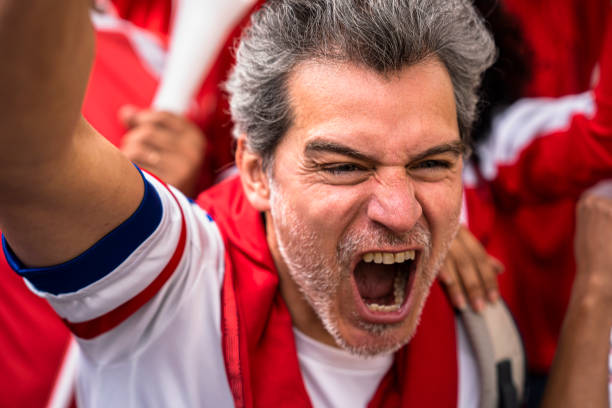 hombre eufórico de mediana edad gritando y celebrando después de que el equipo nacional de fútbol marca gol en un estadio lleno de gente - cántico fotografías e imágenes de stock