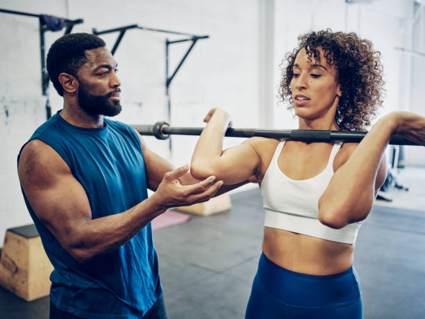 Trainer Working With a Woman in a Gym An athletic trainer in a gym, instructing a woman doing cross training exercise. fitness instructor stock pictures, royalty-free photos & images