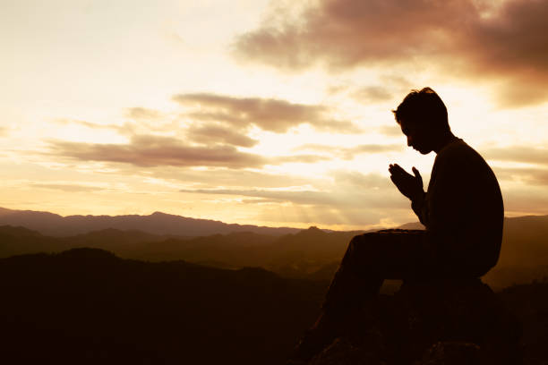 die silhouette eines mannes betet auf dem berg zu gott. betende hände, zollen sie respekt. - praying men god kneeling stock-fotos und bilder