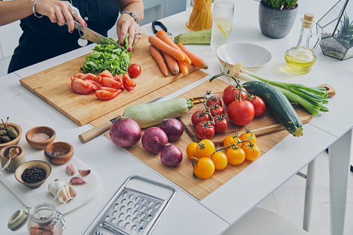 A young adult woman in the kitchen, slicing a lettuce, preparing healthy vegan food salad, close up