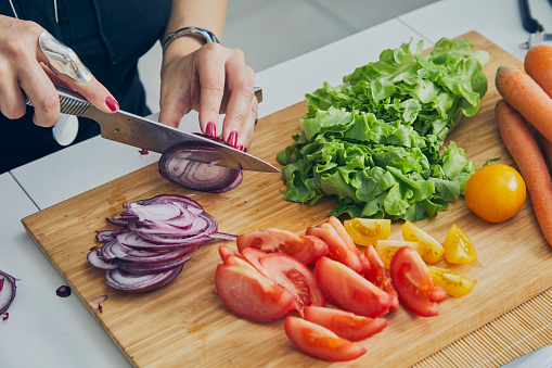 A young adult woman in the kitchen, slicing a Spanish onion, preparing healthy vegan food salad, close up