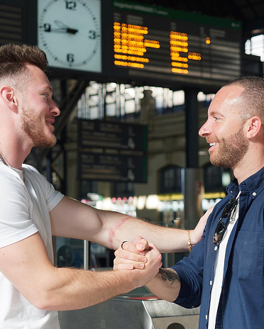 Close up of Two smiling friends shaking hands and saying goodbye at the train station. Travel concept.