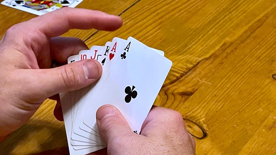 Human hands resting on wooden table holding playing cards, card games leisure activity having fun, pair of Aces different suits of cards in hand.