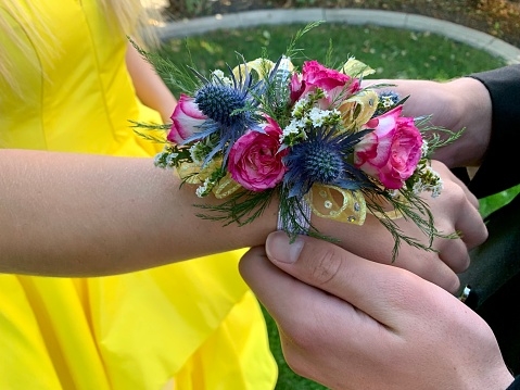Young teenage male, age 17-18, placing beautiful corsage on wrist of Homecoming date. High school traditions celebration events, social etiquette traditions. High school memories, Senior year.