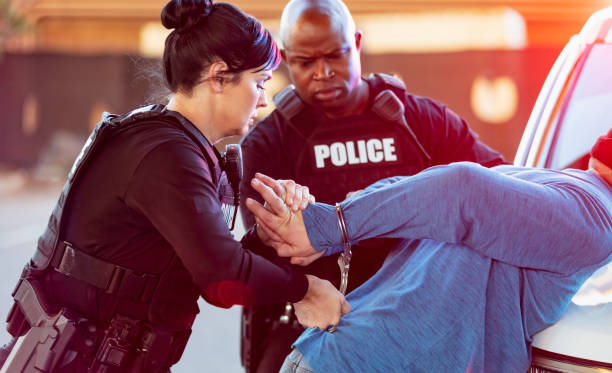 Policewoman and partner, handcuffing man Two multiracial police officers arresting a man. The suspect is leaning on the hood of a patrol car with his hands behind his back, being handcuffed by the policewoman while her African-American partner watches. female police officer stock pictures, royalty-free photos & images