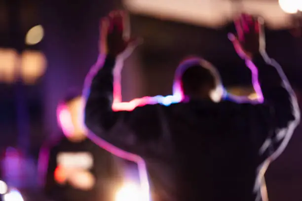 A man with his hands raised, surrendering to police at night. His back is to the camera. A policewoman is standing in the background facing the suspect.