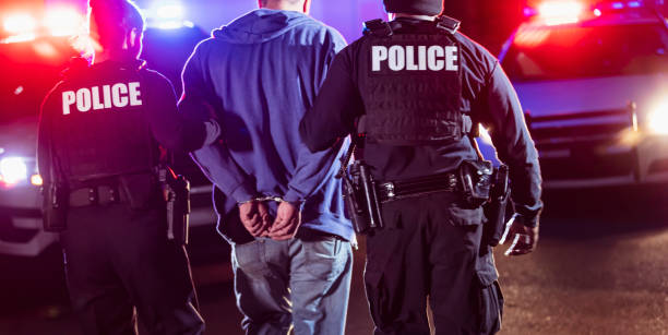 Handcuffed suspect being arrested by police at night stock photo