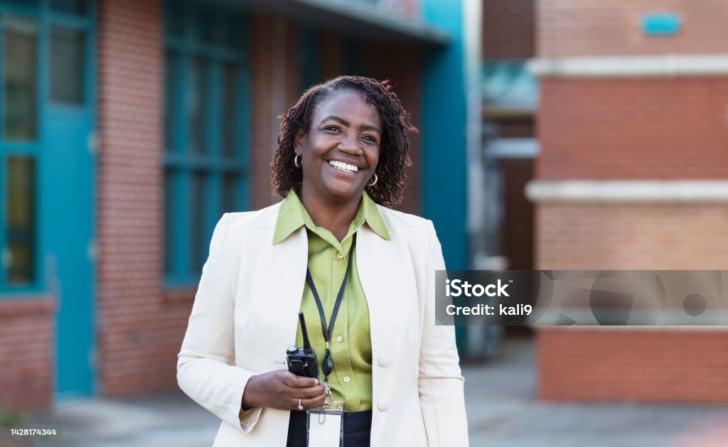 African-American teacher or principal outside school A mature African-American woman standing outside a school building, smiling and looking away from the camera. She is a teacher or school principal. Education Stock Photo