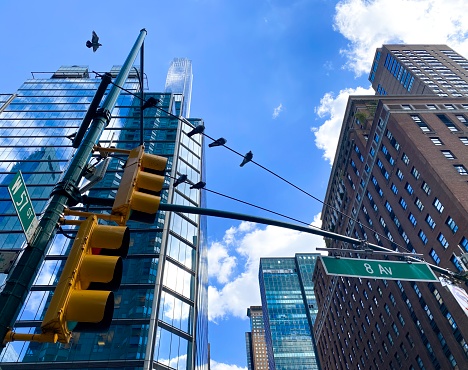 New York, NY, USA - September 27, 2022: The corner of W. 57th St. and 8th Avenue in Manhattan, birds on a wire, blue sky, stoplights and mix of pre-war and modern buildings. Joyful, bright mood.