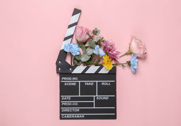Romantic concept. Movie clapperboard with flowers on a pink background. Creative layout. Flat lay stock photo