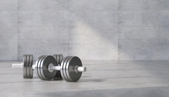 Luxury pair of dumbbell for gym, exercise and sport equipment in modern gray concrete room at home with sunlight from window in background