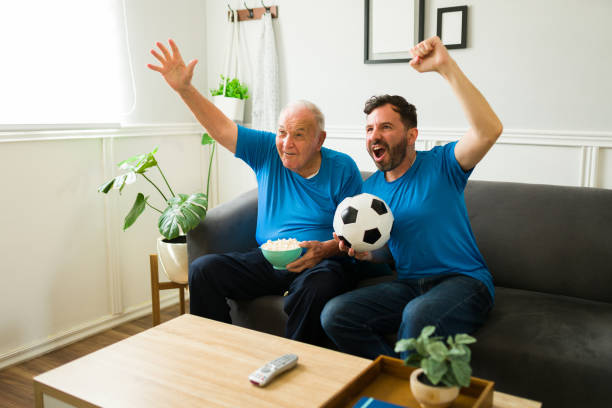 Senior caucasian man shouting and celebrating while watching a soccer game on tv stock photo