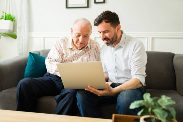 hijo feliz y padre anciano usando la computadora portátil juntos - hijo adulto fotografías e imágenes de stock
