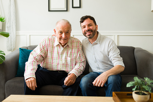 Portrait of a happy elderly senior father hugging his cheerful son while spending time together chatting at home