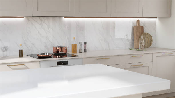 Modern and luxury beige wooden kitchen island and counter with white counter top and glass-ceramic stove top in sunlight from window on marble wall Modern and luxury beige wooden kitchen island and counter with white counter top and glass-ceramic stove top in sunlight from window on marble wall for cooking and dining lifestyle product display quartz stock pictures, royalty-free photos & images