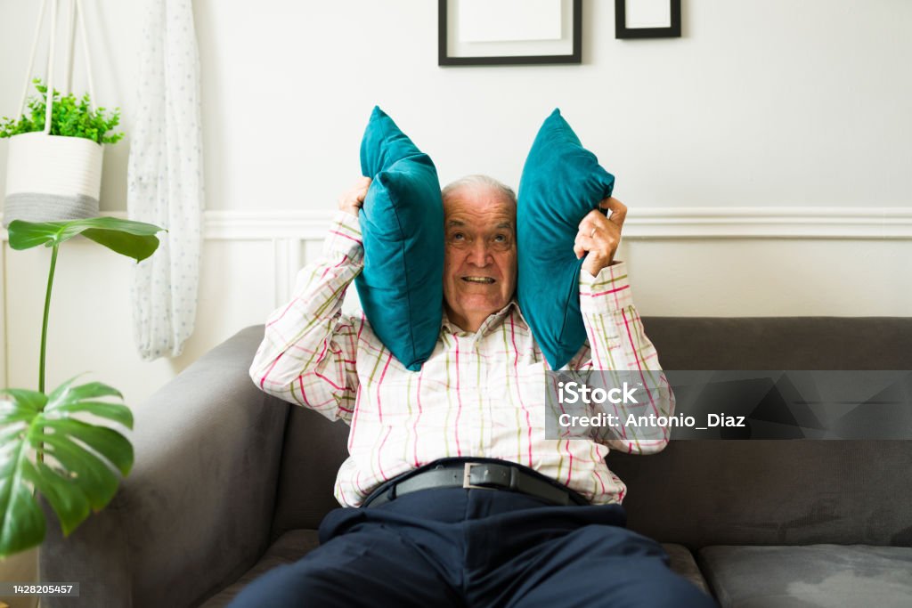 Stressed old man suffering because of the loud music of his neighbors Angry elderly man looking stressed covering his ears because of the loud noise and music from his neighbors Senior Men Stock Photo