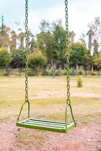 Green swing in an empty park. Close up of a swing that is up in a place full of grass or nature.
