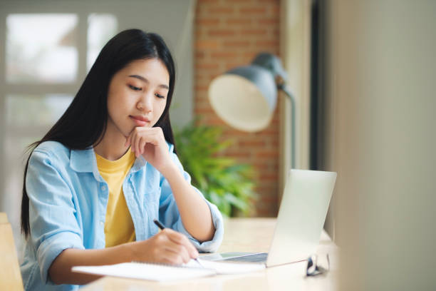 istock Young asian woman sitting at table studying and writing on notebook. 1428218782