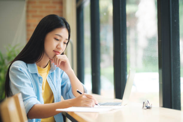 istock Young asian woman sitting at table studying and writing on notebook. 1428218783
