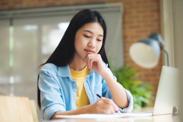 istock Young asian woman sitting at table studying and writing on notebook. 1428219343