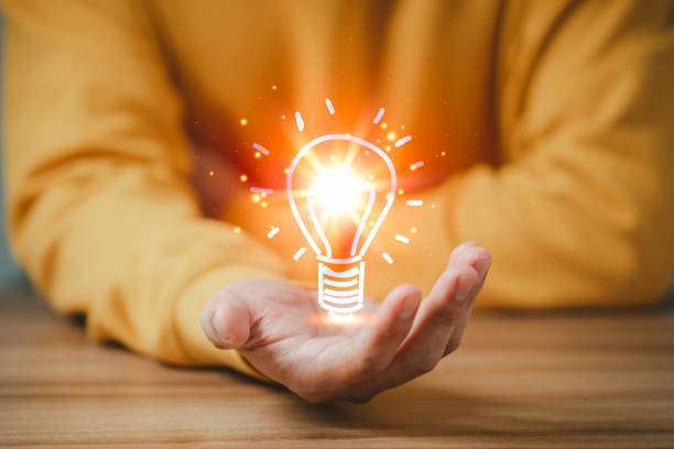 istock Man holding a glowing abstract light bulb on a wooden table, business problem solving ideas and creative marketing ideas Inventing and learning new things. 1428220899