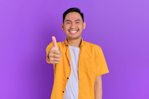 istock Smiling handsome young Asian man showing thumb up gesture, looking at camera isolated on purple background 1428223857