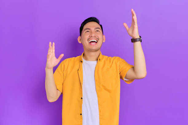 istock Excited handsome young Asian man looking up with a happy expression while raising arms isolated on purple background 1428223888