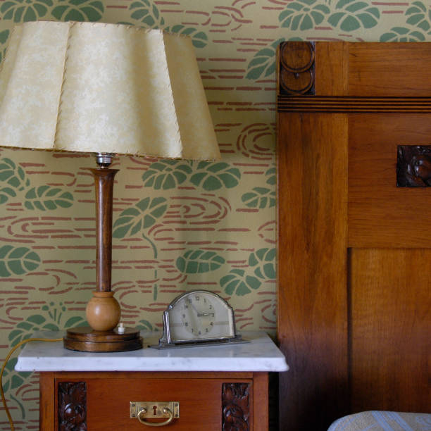 A nostalgic, two-arm wall sconce featuring ornate metalwork and fabric lampshades casts a soft, warm glow on a richly patterned floral wallpaper. Ideal for vintage interior decor, hotel lobby, or boutique settings.