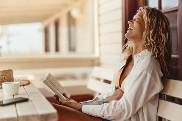 istock Cheerful woman reading a book on a bench at patio. 1428225737