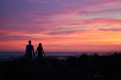 The romantic couple standing on the sea shore on the beautiful sunset background