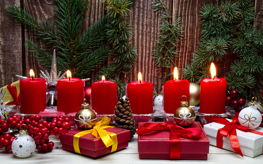 Red Christmas candles and Christmas gift boxes against wooden background