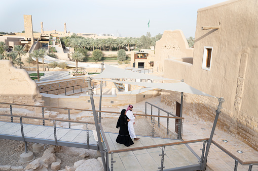 Elevated view of man and woman walking side by side as they explore archaeological site that was first Saudi capital and original home of royal family. Property release attached.