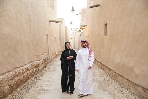 Full length front view of Saudi couple in their 30s wearing traditional attire and admiring buildings in open air museum near Riyadh. Property release attached.