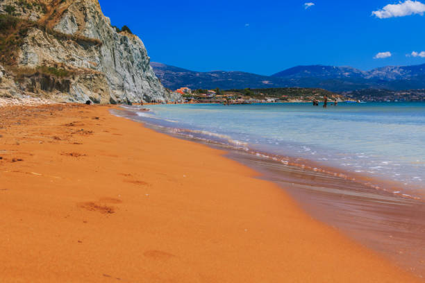 spiaggia di sabbia rossa di xi seduta con montagne e nuvole sullo sfondo sull'isola di cefalonia, in grecia, sotto un cielo blu - greece crete beach island foto e immagini stock