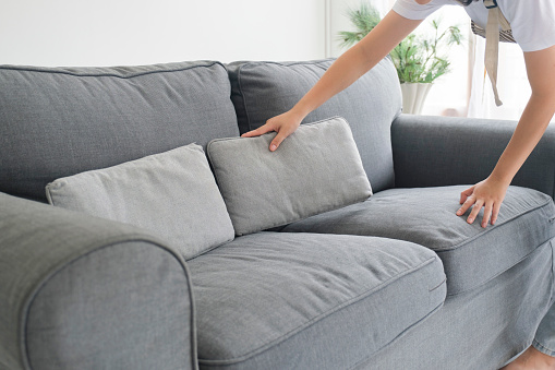 Woman cleaning and arranging sofa cushions in living room at home while doing housechores. Housekeeping concept.