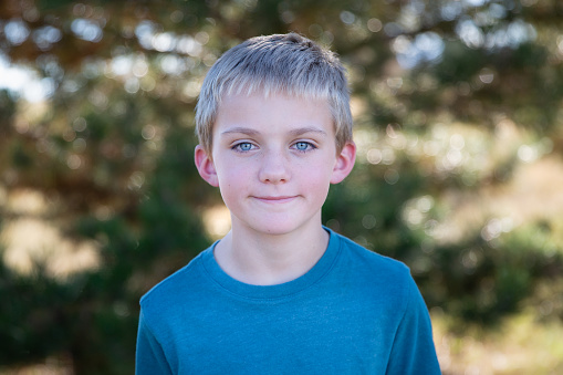 One boy with blue eyes looking at camera outside by a tree