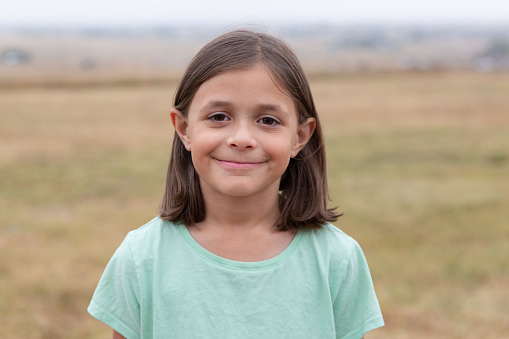Young girl standing outside in a rural field on an overcast day looking directly into the camera.