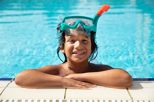 Portrait of smiling little boy enjoying underwater swim in the pool. The boy is gliding by the camera during swimming lesson. Sunny summer day.