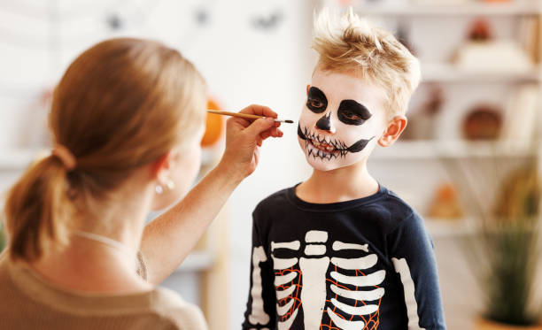 istock Festive makeup for Halloween. Woman doing skeleton make-up for boy in costume while preparing holiday 1428236669