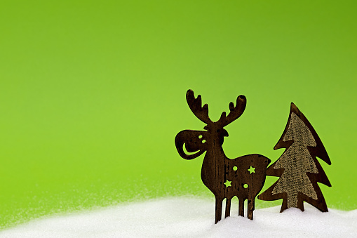 funny reindeer with fir tree, made of tin in the snow on a green background