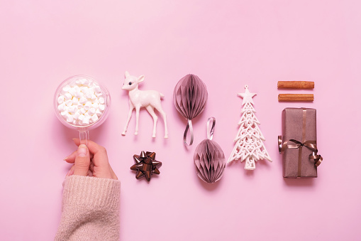 Festive minimal creative christmas composition with gifts, paper balls and female hand with marsh mellow flat lay on pink background.