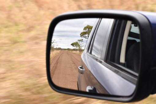 Driving around in the African bush on safari. Driving on the open gravel road. Driving on a long road. Raining in the African bush with dark clouds forming. The river running fast after the rains. Looking into the rearview mirror of the vehicle and observing the road in the bush.